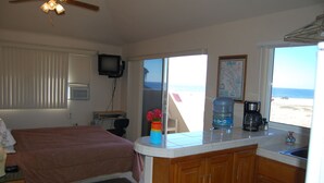 Une chambre à coucher avec un lit, un petit bureau, une télévision et une fenêtre donnant sur la plage.