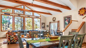A spacious living area with a wooden ceiling, large windows, and a dining table with chairs. - Healing House - fireplace, wifi, 2 kings, furnished den, screen porch, pool access (Berkeley Springs)