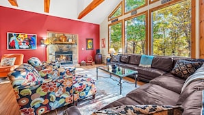 A spacious living room with a fireplace, large windows, and a vibrant red accent wall. - Healing House - fireplace, wifi, 2 kings, furnished den, screen porch, pool access (Berkeley Springs)