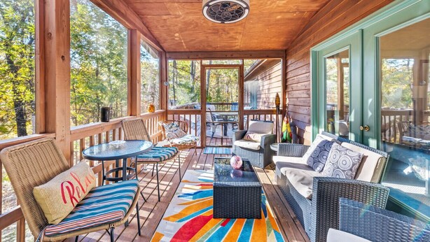 A covered porch with wicker furniture, a colorful rug, and a view of the surrounding trees. - Healing House - fireplace, wifi, 2 kings, furnished den, screen porch, pool access (Berkeley Springs)