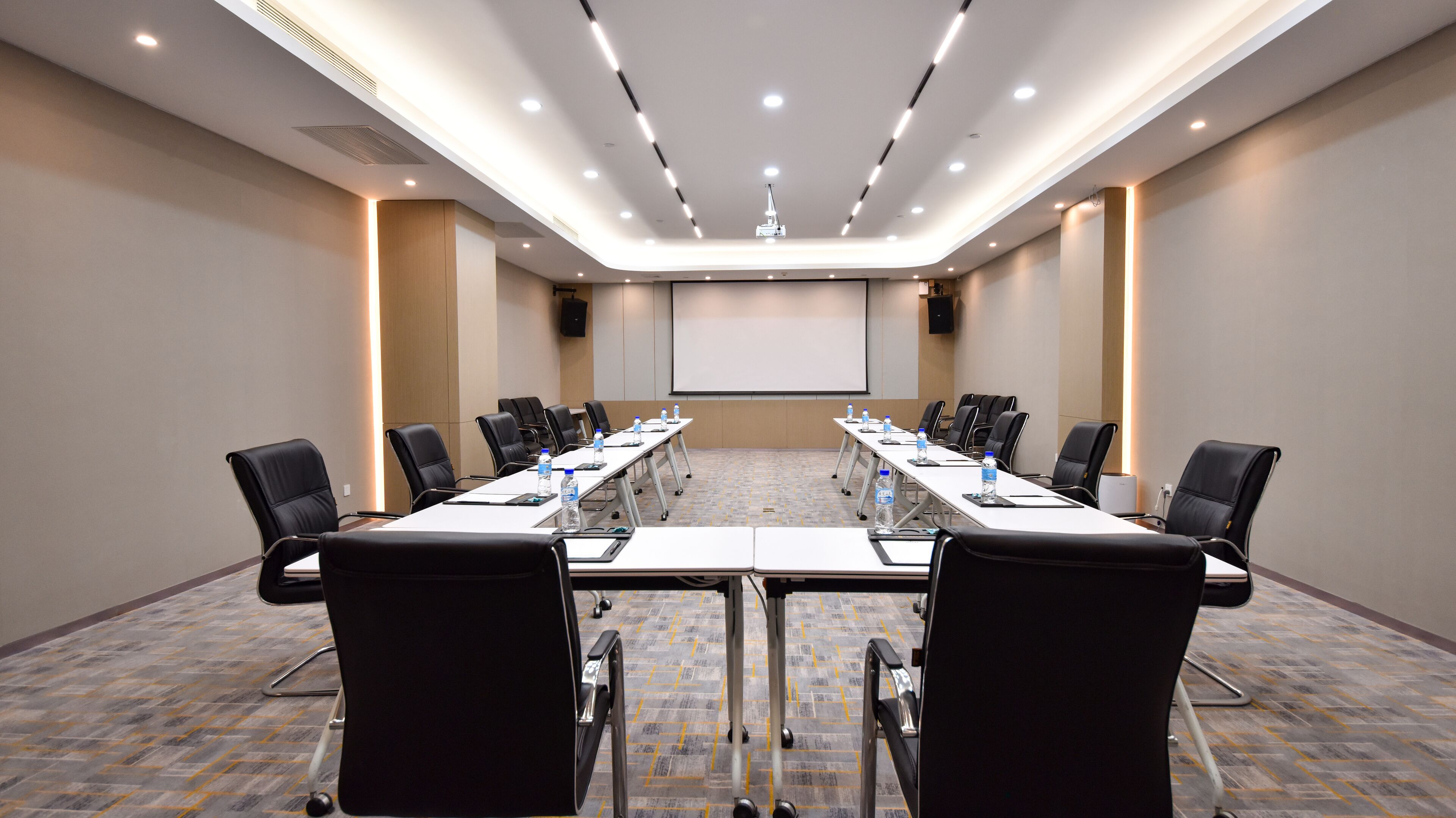 A conference room with a long table, black chairs, and a projector screen.