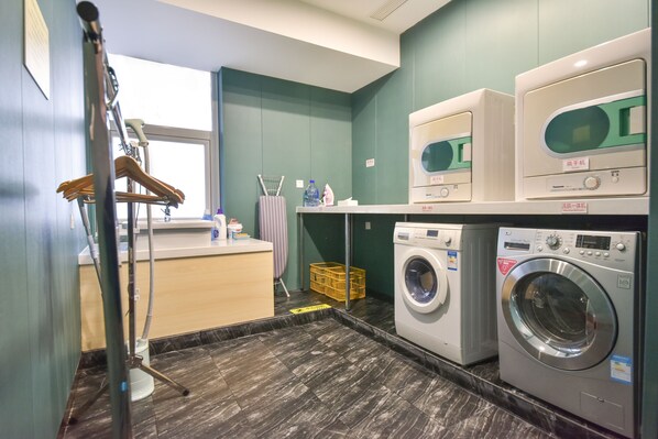 A laundry room with two washing machines, a drying rack, and a small table with cleaning supplies. - Yantai Asia Hotel (Yantai)