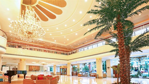 A spacious lobby with a grand chandelier, a piano, comfortable seating, and a palm tree centerpiece. - Yantai Asia Hotel (Yantai)