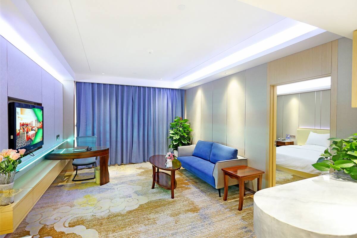 Una habitación de hotel moderna con televisión de pantalla plana, un sofá, una cama, una mesita y una planta en maceta.