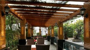 An outdoor covered patio with wooden beams, wicker furniture, and potted plants. - Gem Flower Jinyu Sunshine Hotel (Chengdu)