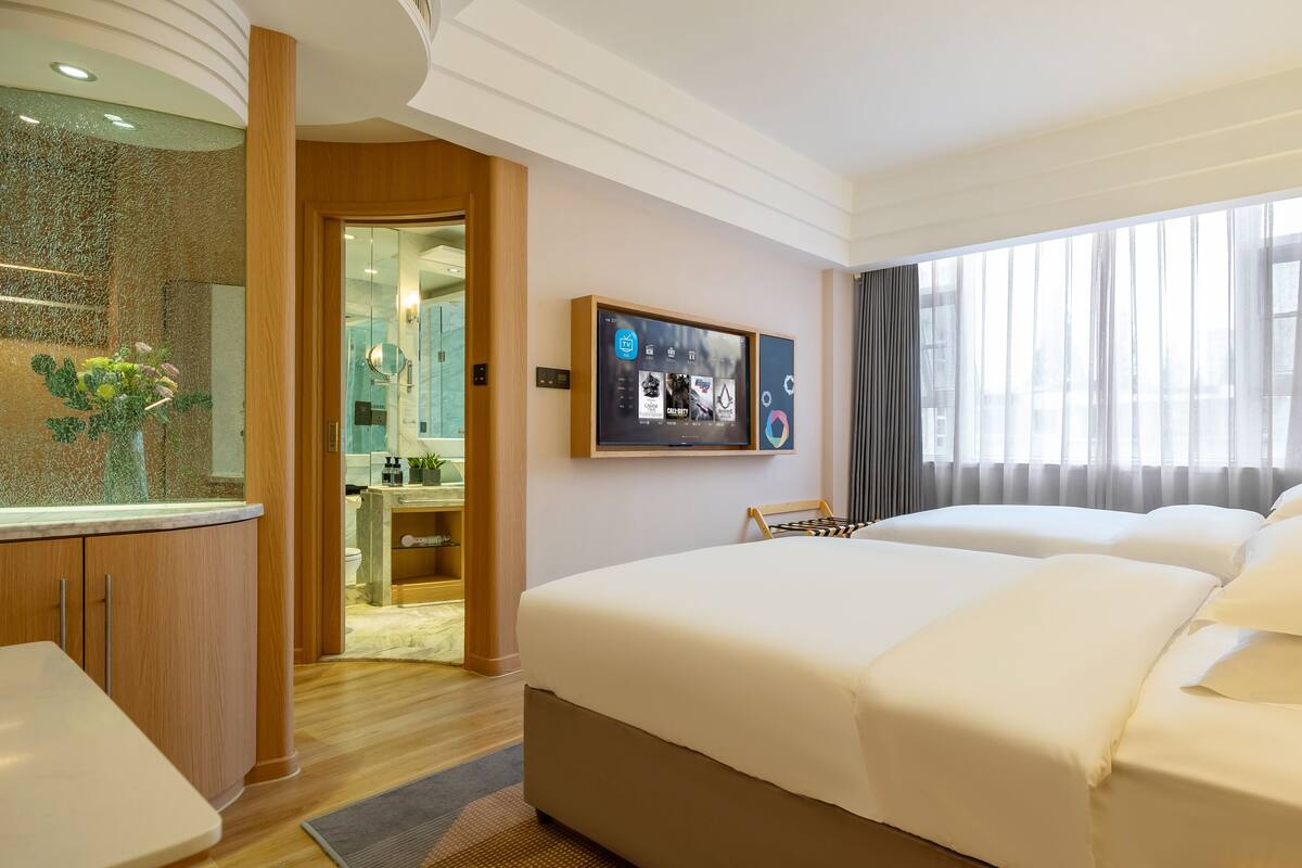 Ein Hotelzimmer mit einem großen Bett, einem an der Wand montierten Fernseher und einem durchgegangenen Tür erkennbaren Badezimmer.
