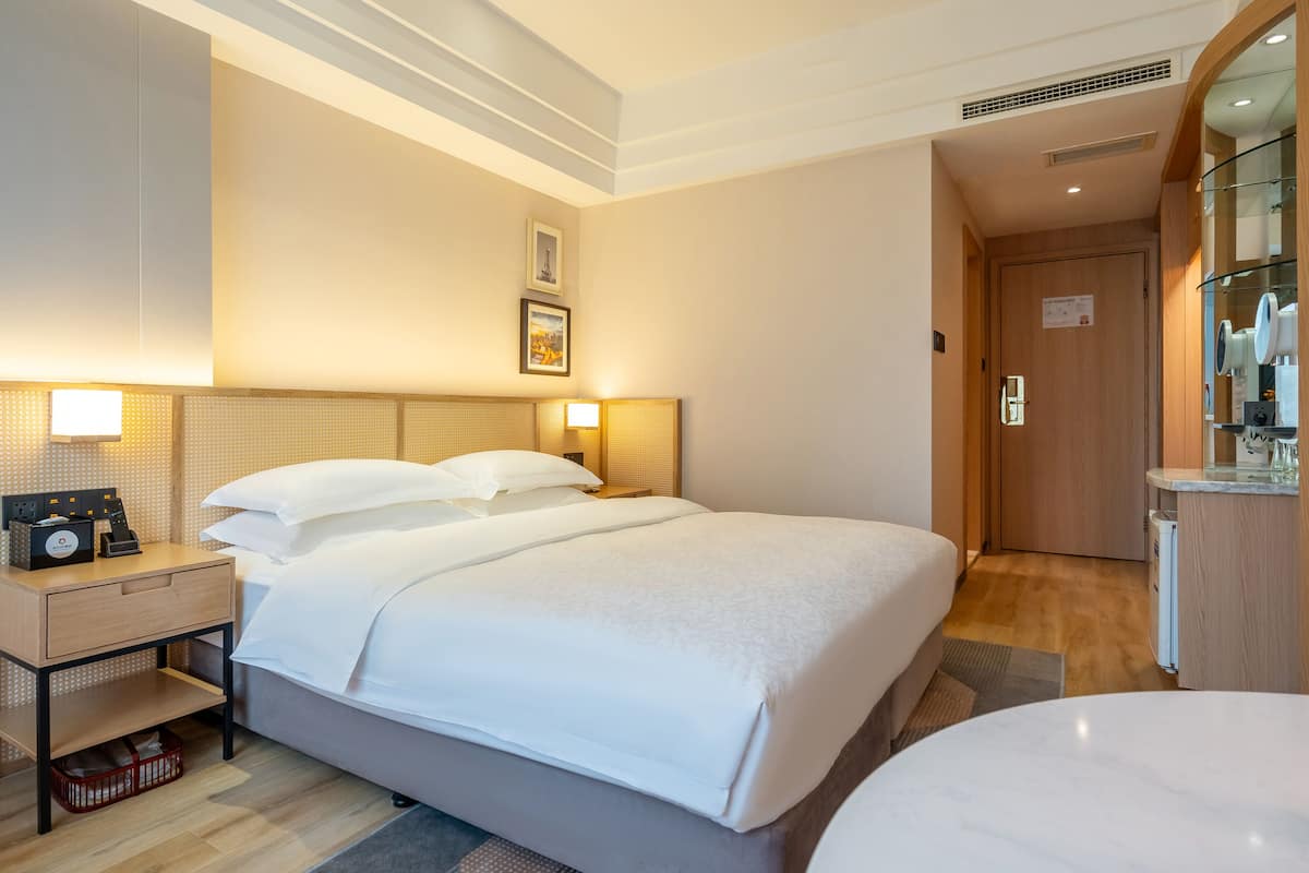 Ein Hotelzimmer mit Bett, Nachttischen, einem Spiegel und einem kleinen Schreibtisch mit Kaffeemaschine.