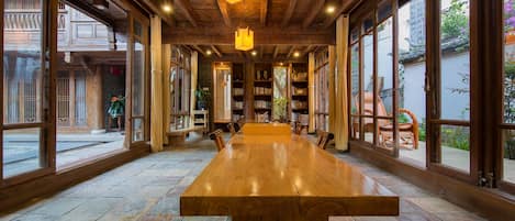 Una habitación amplia con una larga mesa de madera, ventanas grandes y estanterías.