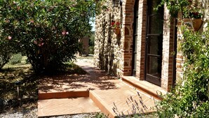 Un edificio de piedra con fachada de ladrillo, un patio empedrado y un jardín con plantas en flor.