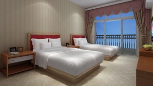 A hotel room with two beds, a nightstand with a phone, a small table with a bowl of flowers, and a balcony with a railing.
