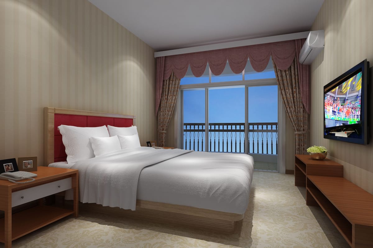 Une chambre d’hôtel avec un grand lit, un téléviseur fixé au mur, une table de chevet, une petite table et une vue sur le balcon extérieur.