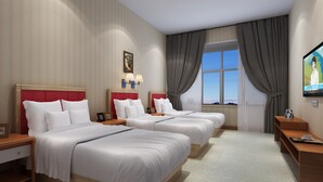 A hotel room with three beds, a TV, and a window with curtains.