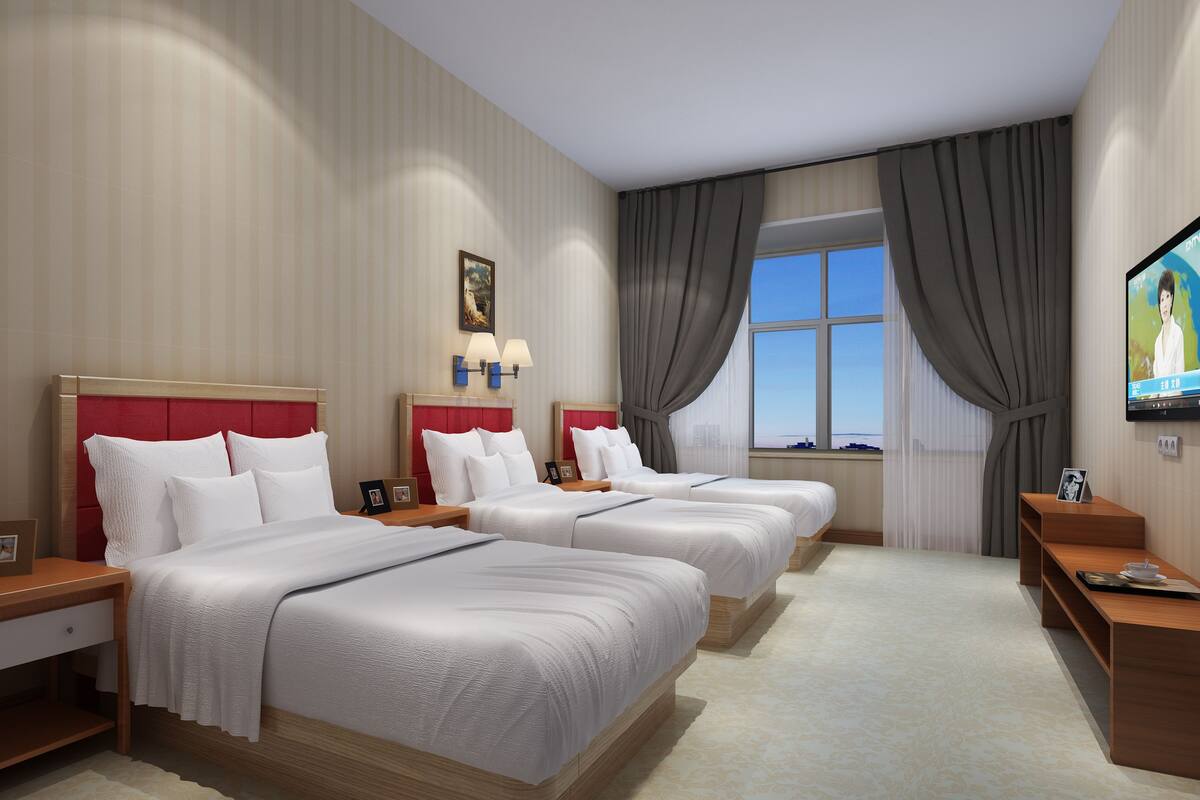 Une chambre d’hôtel avec trois lits, une télévision et une fenêtre avec des rideaux.