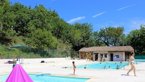 Zona de piscina con un edificio pequeño, sillas de descanso y una carpa.