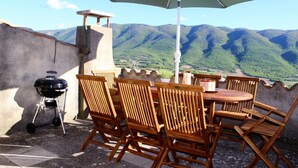 Un patio con sillas y una mesa de madera, una parrilla y un paraguas grande.