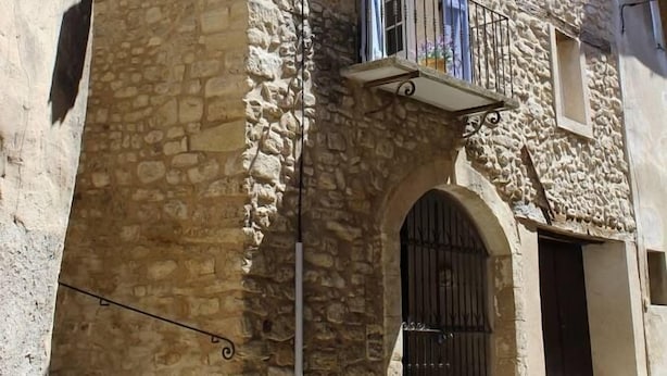 Un edificio de piedra con balcón, arco de entrada y varias ventanas con persianas.