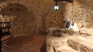Una habitación con paredes de piedra, suelo de baldosas, un banco de piedra y un farol colgante.