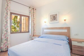 A bedroom with a bed, a nightstand, a wall-mounted light, and a window with curtains. - Villa Maryvilla - AFRODITA (Calp)