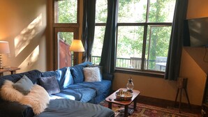 A cozy living room with a blue sofa, a patterned rug, and a table with a lamp and a lantern. - The Wild Mile River Retreat (Bigfork)