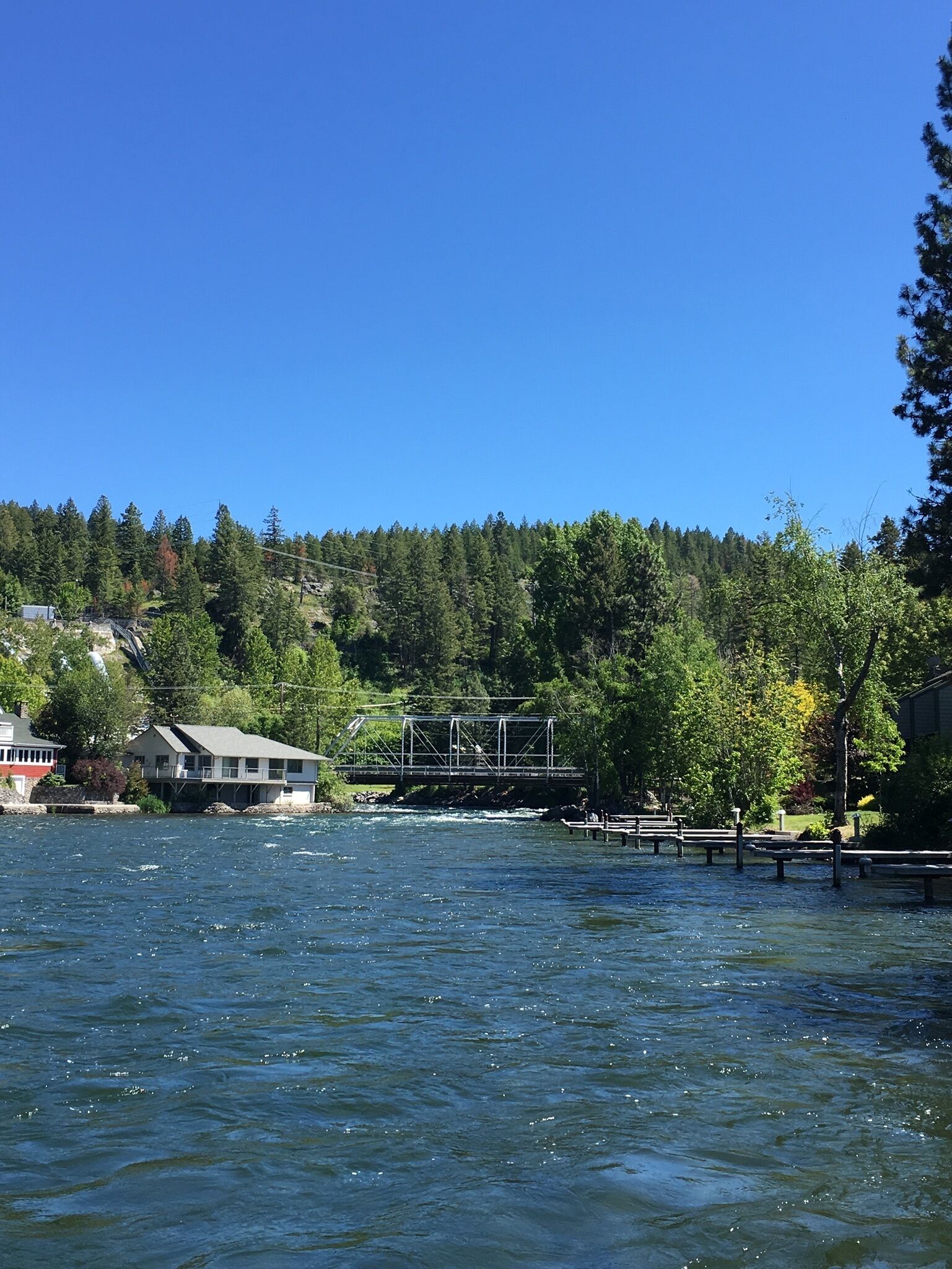 Une rivière traversée par un pont, une maison au bord de l’eau et une colline boisée.