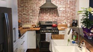 A kitchen with a brick wall, a stainless steel range hood, a stove, a sink, and wooden countertops. - The Wild Mile River Retreat (Bigfork)