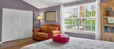 A bedroom with a bed, a ceiling fan, a window with blinds, a door, and a chair.