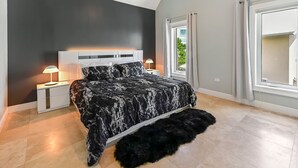 A bedroom with a bed, bedside tables, a large window, and a view of greenery outside.