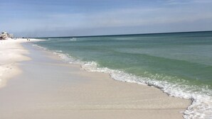 Ein Strand mit klarem Wasser, einem sandigen Ufer und einigen Gebäuden im Hintergrund.