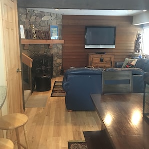 A living room with a stone wall, wooden paneling, a flat-screen TV, a blue sofa, a wooden coffee table, and a small wooden cabinet.
