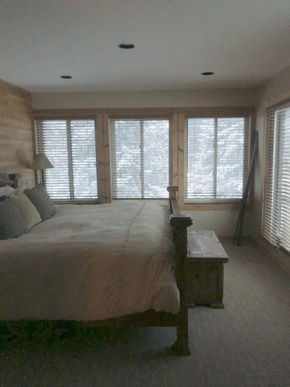 A bedroom with a large bed, a nightstand, and a window with blinds.