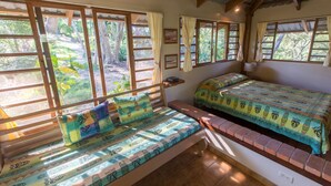 A room with two beds, a bench, and large windows with curtains.