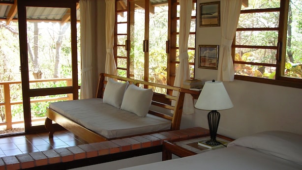 A bedroom with a wooden bed, a nightstand with a lamp, and a window with curtains.