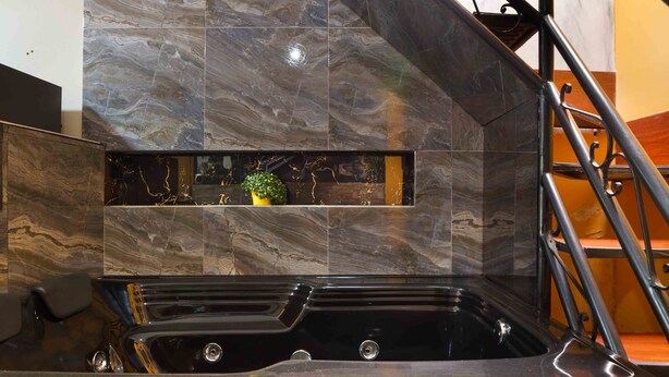 Un baño moderno con una bañera negra, baldosas de mármol y una pequeña planta en la pared.