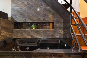 A modern bathroom with a black bathtub, marble tiles, and a small plant on the wall.