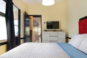 A hotel room with a bed, a TV on a dresser, and a view of the hallway.