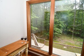 Une pièce dotée d’une grande fenêtre donnant sur une zone boisée. On y trouve un banc en bois sur lequel sont posés deux verres de vin rouge.