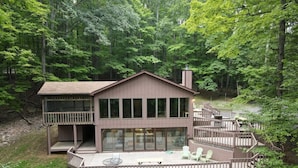 A cabin with a deck, large windows, and a chimney.