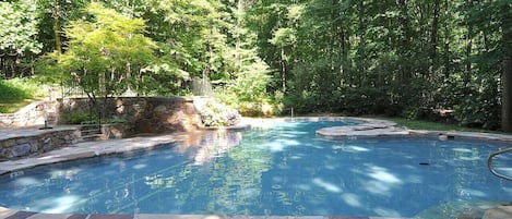 A swimming pool with stone tiles, surrounded by lush greenery and trees.
