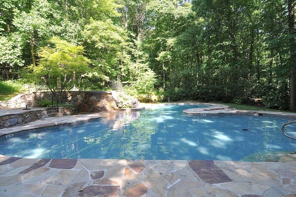 A swimming pool with stone tiles, surrounded by lush greenery and trees.