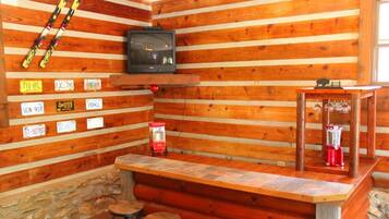 A log cabin interior with a bar area, stone wall, and a television mounted on the wall.