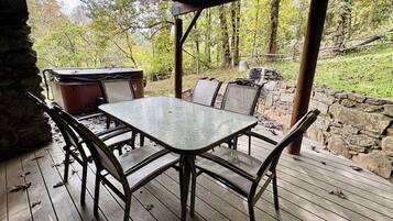 An outdoor patio with a glass-top table and metal chairs, surrounded by a stone wall and a wooden deck.