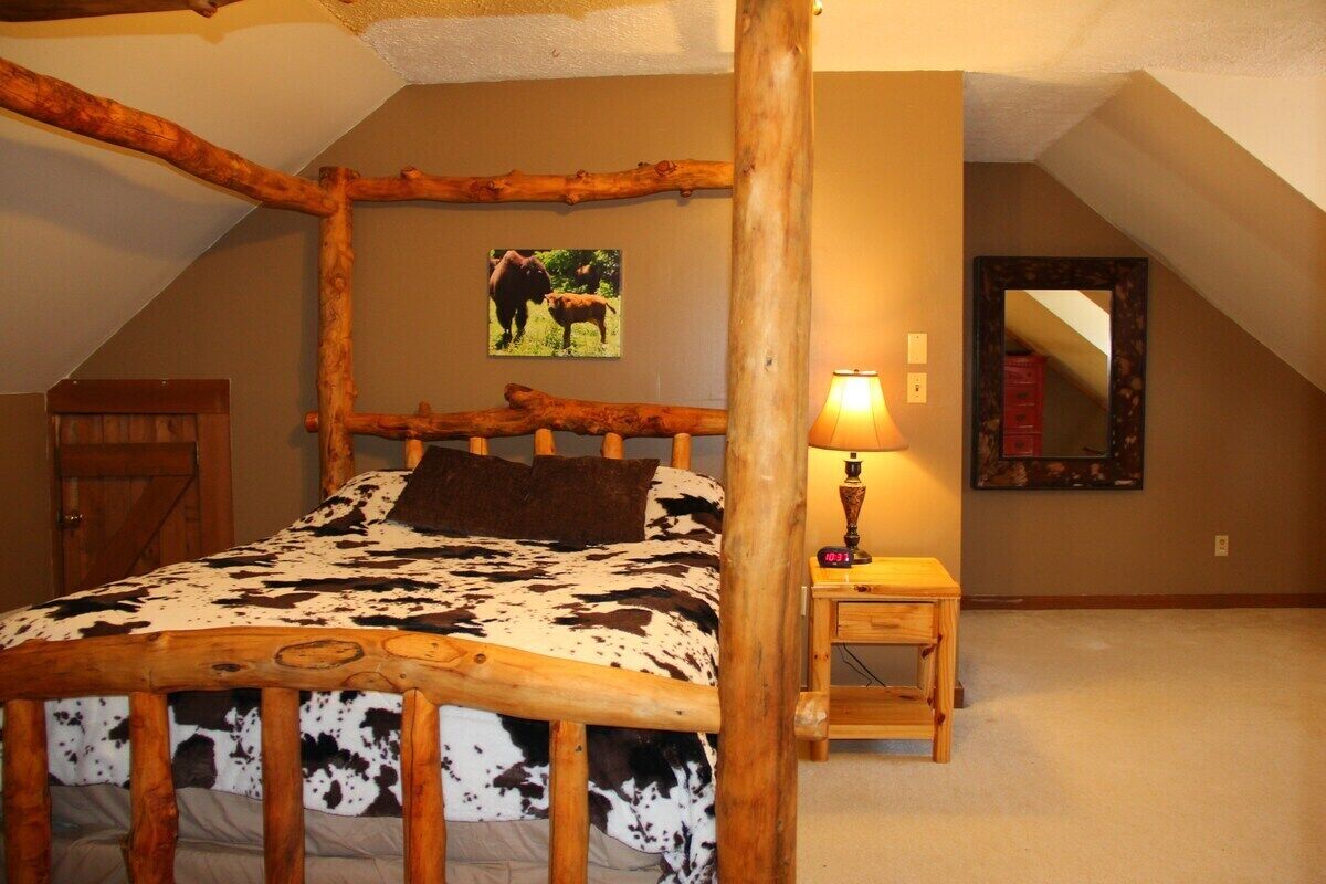 Une chambre à coucher avec un lit à baldaquin en bois, une petite table de chevet avec une lampe, un tableau encadré au mur et un miroir.
