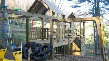 A wooden play structure with a swing set and tire swings.