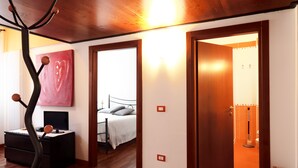 Ein Schlafzimmer mit einem Bett, einem Nachttisch und einem Gemälde. Eine Tür führt in einen anderen Raum.
