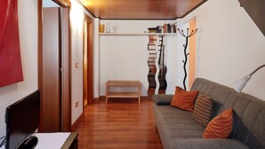 Ein modernes Wohnzimmer mit grauem Sofa, Holzboden, einer kleinen Holzbank und einem Fernseher auf einem Schrank.