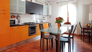 Eine moderne Küche mit orangefarbenen Schränken, einem Glastisch und Blick ins Freie.