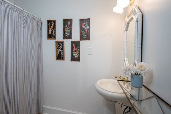 A bathroom with a striped shower curtain, a sink with a mirror, and five framed pictures on the wall.