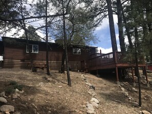 Un chalet rustique doté d’une terrasse en bois et d’un sentier de terre menant à l’entrée.