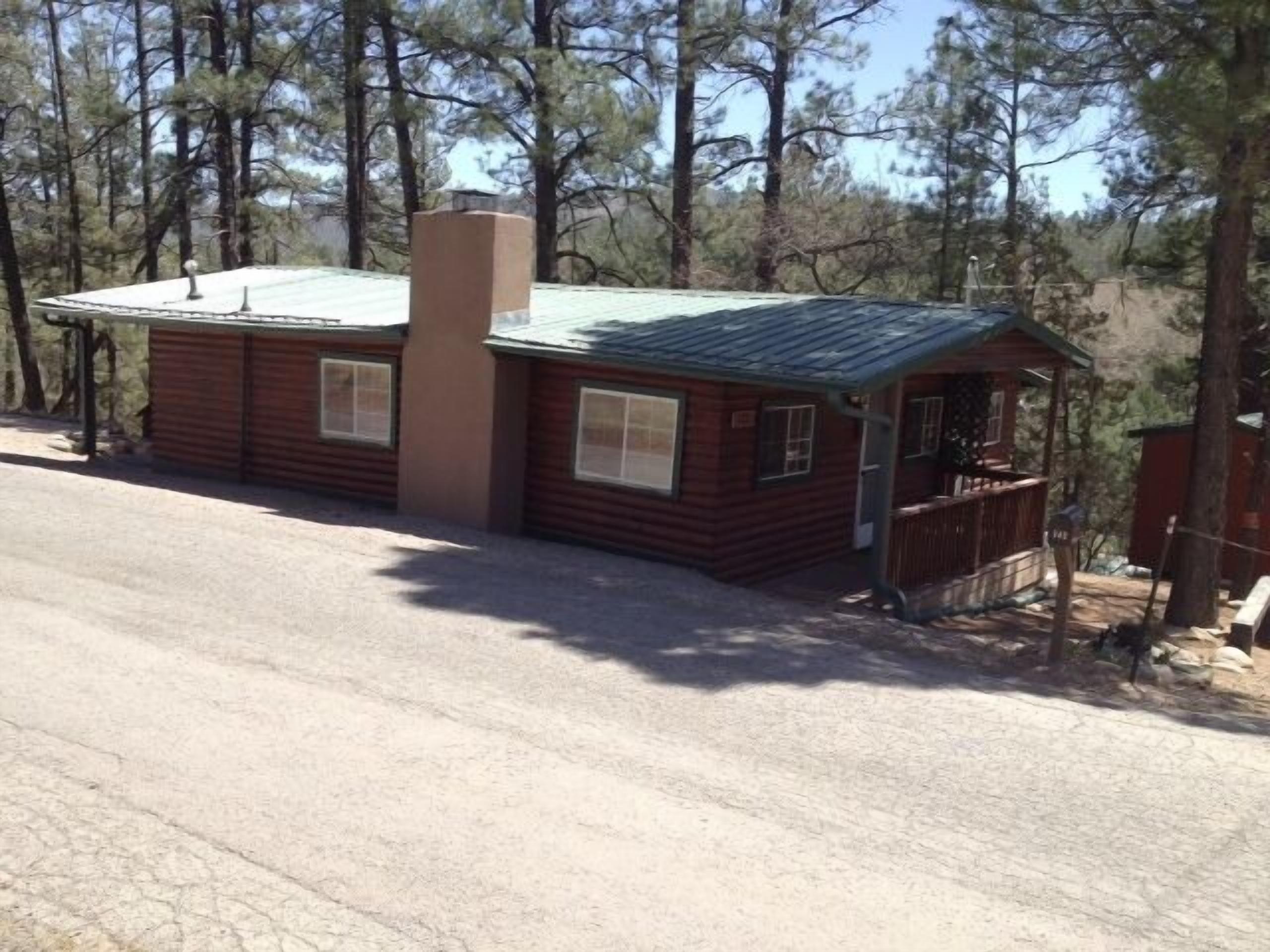A small, single-story cabin with a green roof, surrounded by trees.