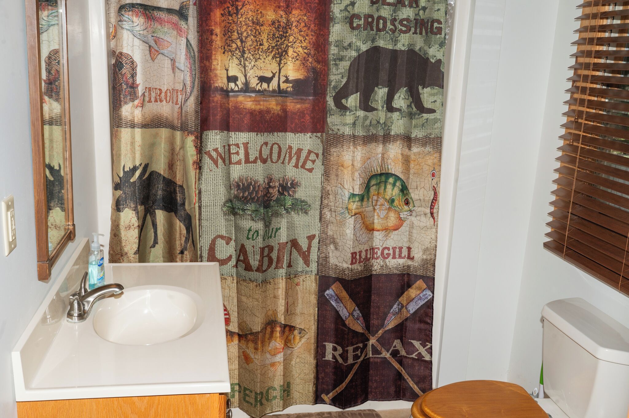 Un baño con lavamanos, inodoro y cortina de ducha con motivos de fauna y pesca.